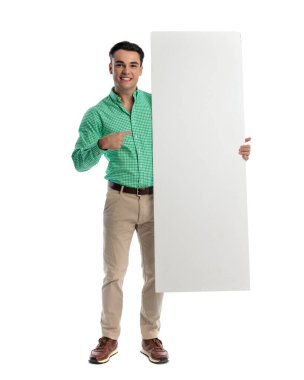 Neşeli genç adam beyaz arka planda ilerlerken boş bir tahtayı işaret ediyor.