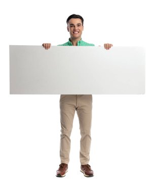 Mutlu sıradan bir adam iki eliyle büyük boş bir tahta tutuyor ve beyaz arka planda ileriye bakarken gülümsüyor.