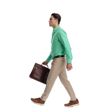 Beyaz arka planda tek başına ileri doğru yürürken elinde deri bir çantayla şık giyinmiş kararlı bir adamın yan görüntüsü.
