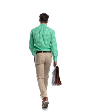 Beyaz arka planda tek başına yürürken elinde deri bir çantayla gezen profesyonel bir adamın arkadan görünüşü.