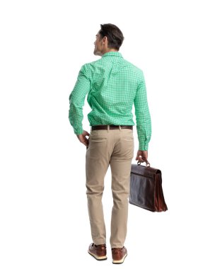 Modern bir adam kareli gömlek giyer ve beyaz arka planda izole bir şekilde cebine uzanırken yan tarafa bakar.