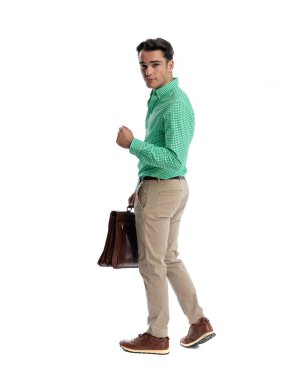 Hırslı işadamı, elinde deri bir çantayla beyaz arka plandaki kameraya bakmak için geri çekiliyor.