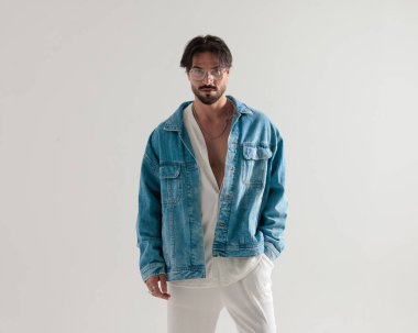 Kot ceketli ve beyaz pantolonlu havalı adam kendine güveniyor ve açık gri arka planda bekliyor.