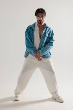 Kot ceketli modaya uygun bir adam el ele tutuşuyor ve açık gri arka planı bekliyor.