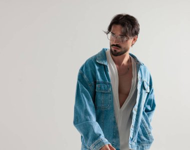 Kot ceketli sıradan dalgın adam açık gri arka planda yana bakıyor.