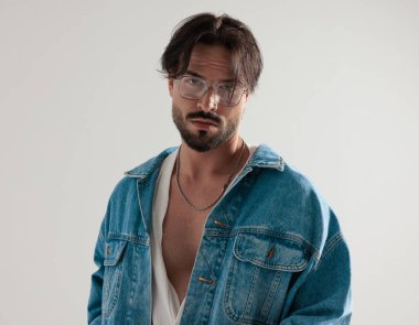 Açık gri arkaplanda ileriye bakan, kot ceketli rahat bir adamın portresi.