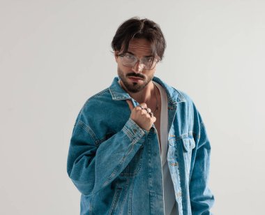 Kot ceketli ciddi bir adam ceketini ayarlıyor ve açık gri arka planı bekliyor.