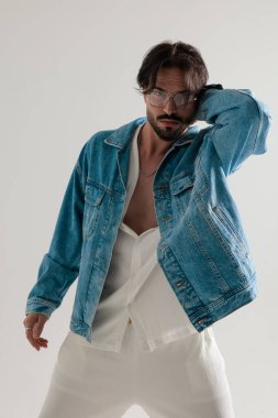 Kot ceketli şık sıradan bir adam başının arkasında el ele tutuşup açık gri arka plandaki kameraya bakıyor.