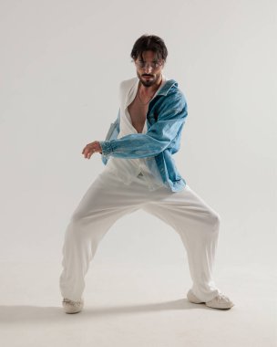 Kot ceketli sıradan adam kolları açık gri arka planda dinamik bir şekilde dans ediyor.