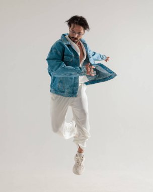 Kot ceketli şık adam havaya atlıyor ve açık gri arka plana bakıyor.