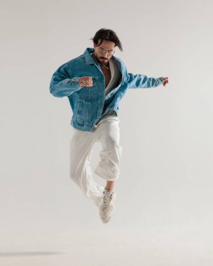 Kot ceketli şık adam açık gri arka planda kollarını açmış havaya zıplıyor.