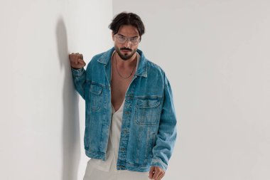 Kot ceketli şık sıradan bir adam beyaz bir duvara yaslanıyor ve açık gri bir arkaplan bekliyor.