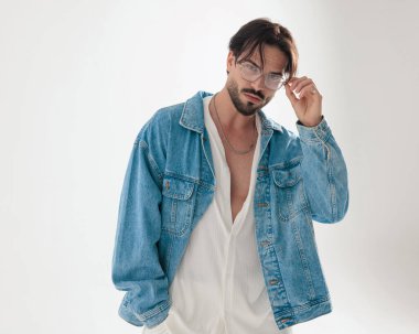 Kot ceketli yakışıklı sıradan bir adam gözlük takıyor ve açık gri arka planda ileriye bakıyor.