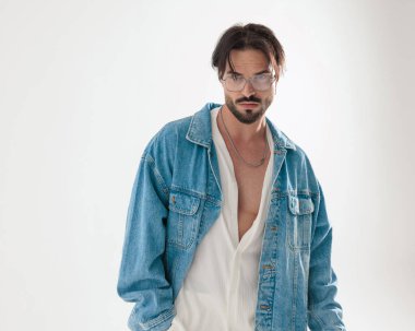 Kot ceketli ciddi modacı, açık gri arka planda el ele duran gözlüklere bakıyor.