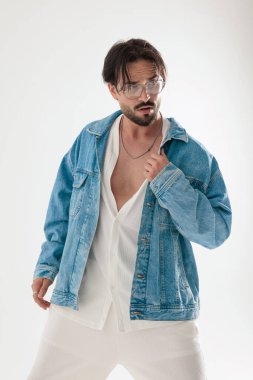 Kot ceketli sıradan moda adamı ceketini tutuyor ve açık gri arka planda yer almak istiyor.