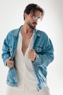 Düşünceli sakallı adam beyaz arka plana bakarken kot ceket tutuyor.