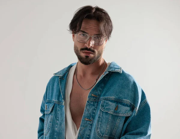 Açık gri arkaplanda ileriye bakan, kot ceketli rahat bir adamın portresi.