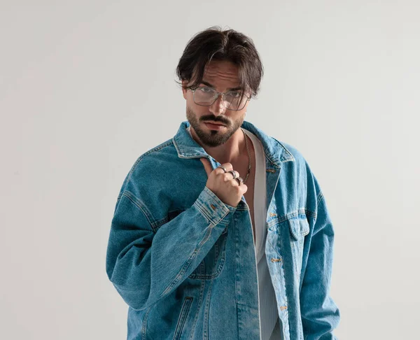 Kot ceketli ciddi bir adam ceketini ayarlıyor ve açık gri arka planı bekliyor.