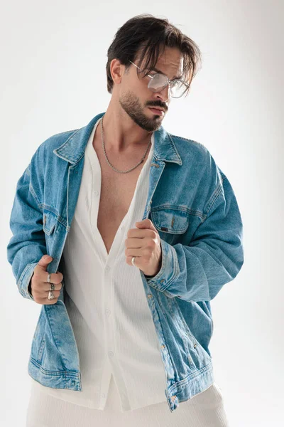 Düşünceli sakallı adam beyaz arka plana bakarken kot ceket tutuyor.