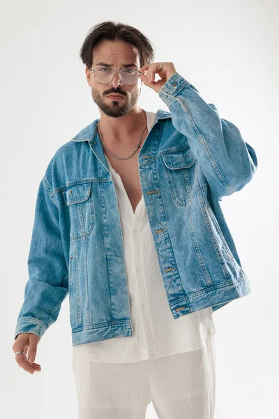 Kot ceketli havalı adam gözlüğü beyaz arka planda ayarlıyor.