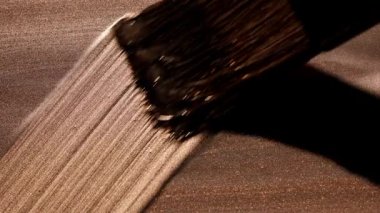 Boya fırçasının dinamik yakın çekimi altın boya yüzeyi boyunca çapraz çizgiler süpürüyor, fırçayla bırakılan ince doğrusal dokuyu vurguluyor ve eylemi kaldırıyor.