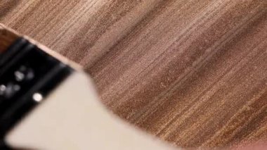 Makro çekim geniş fırça darbelerini göstererek üst üste binen çapraz doku oluşturur, bu da altın boyanın kumaş benzeri görünümü ile sonuçlanır..