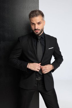 Siyah takım elbiseli odaklanmış moda işadamı siyah beyaz arka planda düğme ceketini ilikliyor.