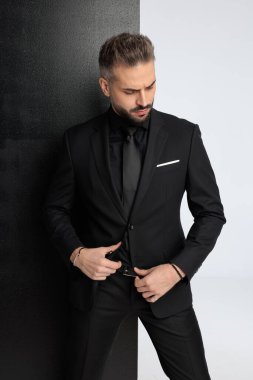 Siyah takım elbiseli dalgın bir iş adamı siyah ve beyaz arka plandaki ayar ceketine bakıyor.