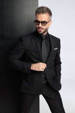 Siyah takım elbiseli modern adam siyah beyaz arka plana bakarken ceket düğmesini ayarlıyor.
