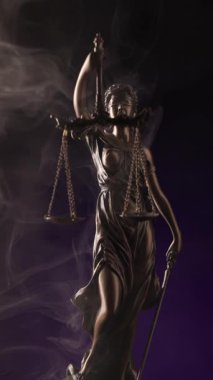 Bronz tenli Justitia figürü yükselen dumanın ortasında duruyor, elinde bir kılıç ve dengeleyici teraziler koyu mor arka plandaki hukuki tarafsızlığı simgeliyor..