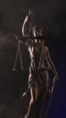 Gözleri bağlı Adalet Anıtı 'nın elinde terazi ve bir kılıç kırmızı ışıklı, koyu bir arka planda dalgalı bir dumanın içinde duruyor..