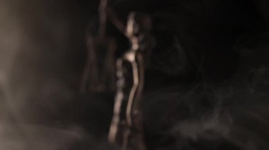 Kamera, elinde terazi tutan bir Adalet Heykeli 'nin detaylarını ortaya çıkarmak için yer değiştirmeden önce bronz bir figürün etrafında dramatik dumanlar uçuşuyor..