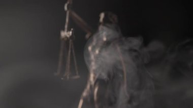 Mercek yer değiştirmeden önce bulanık bronz bir figür etrafında dönen kalın beyaz sis adaletin asılı pullarının detaylarını netleştirmek için odaklanır..