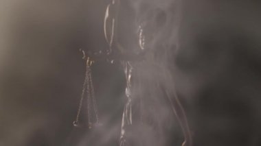 Bronz Adalet Heykeli elinde terazi ve koyu bir arka planda kalın dumanla çevrili bir kılıç tutuyor..