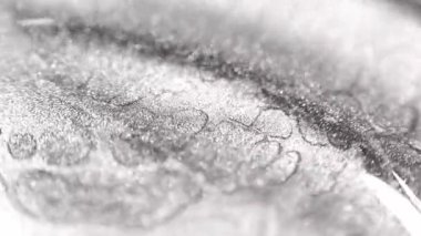 Özel kumlu deseni olan gümüş platin renkli makro boya ağır dalgalara ve tepelere doğru akarken ışıl ışıl ışıl parlayan parçacıklar ışıkta kayıyor ve siyah arkaplanda derin bir kontrastı ortaya koyuyor.