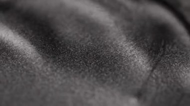 Koyu gümüş metalik sıvı yüzeyin büyüleyici yakın çekimi yumuşak dalgalarla dalgalanır ve kumlu dokuda kayan ışık parıldayan titanyum parçacıkları ve kadife desenleri ortaya çıkarır.