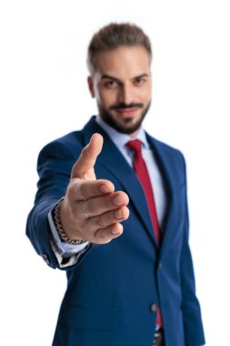 Welcoming businessman in a blue suit reaching out to shake hands while looking forward isolated on white background