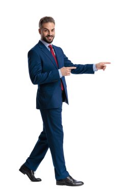Side view of happy businessman walking and pointing fingers to side while looking forward isolated on white background