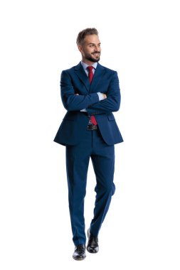 Stylish man in blue suit crossing arms and looking to side on white background