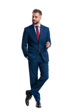 Skeptical businessman crossing legs and looking to side while standing on white background