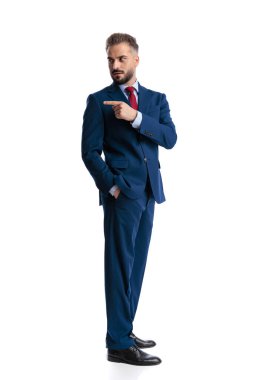 Handsome businessman pointing finger to the side and looking away over shoulder while holding hand in pocket isolated on white background
