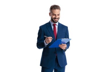 Neşeli iş adamı elinde kalem tutarken ve mavi bir panoya notlar yazarken beyaz arka planda izole edilmiş bir gülümsemeyle aşağıya bakıyor.