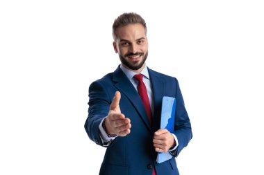 Welcoming businessman in blue suit holding clipboard and extending hand for handshake looking forward isolated on white background