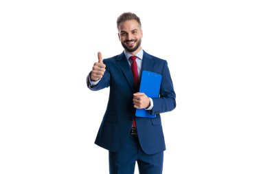 Positive businessman in blue suit holding clipboard and making thumbs up gesture looking forward isolated on white background