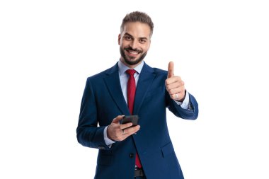 Mavi takım elbiseli, akıllı telefon tutan, gülümseyen ve beyaz arka planda ileriye bakan pozitif iş adamı.