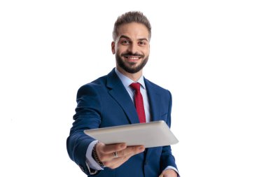 Mavi takım elbise giyen mutlu işadamı beyaz arka planda sırıtırken dijital tablet sunuyor.