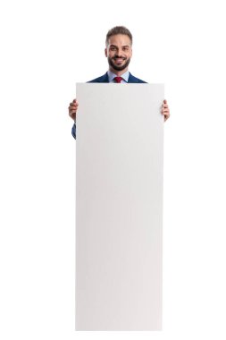 Mavi takım elbiseli mutlu profesyonel adam reklam için uzun beyaz bir levha tutuyor ve beyaz arka planda ileriye bakıyor.
