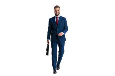 Happy man wearing blue suit walking forward and holding briefcase with smile while looking forward on white background