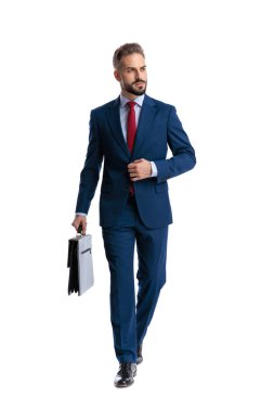 Zarif iş adamı evrak çantası tutuyor ve beyaz arka planda yürürken ceketini ayarlıyor.