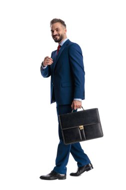 Neşeli iş adamı evrak çantasını tutuyor, parmakla işaret ediyor ve beyaz arka planda izole bir şekilde ileriye bakıyor.